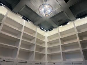 Luxury custom-built floor-to-ceiling shelving with cabinet storage, featuring a coffered ceiling and modern lighting. A perfect example of how expert craftsmanship and high-quality materials elevate a space—because in custom carpentry, quality always wins over price.