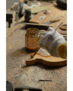 A person applying a rich brown wood stain with a brush on a light-colored wooden surface, highlighting the natural wood grain. CFL Custom Carpentry ensures the best wood finishes for durability and elegance.