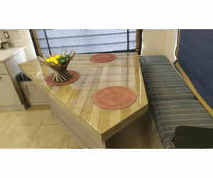 A dining area with striped blue upholstered custom banquettes and a glossy wood dining table, decorated with red round placemats and a modern fruit holder centerpiece.